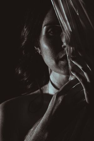 Dramatic black and white portrait through translucent material creating ethereal shadows and highlights.