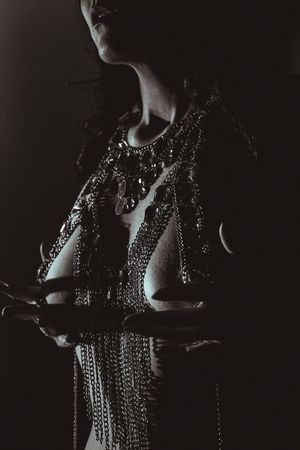Dramatic artistic portrait featuring intricate beaded jewelry and chains in moody low-key lighting with dark shadows.