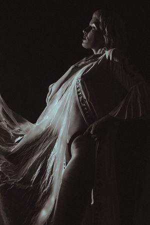 Dramatic black and white artistic portrait showing a figure in flowing white fabric against dark background.