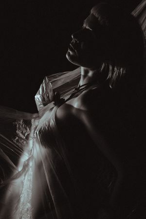 Moody monochrome portrait in low key lighting showcasing delicate fabric draping and shadows.
