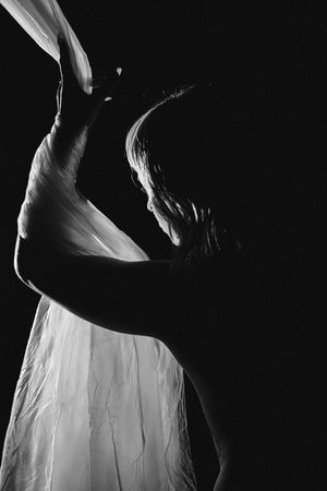 Artistic black and white silhouette photograph of a figure with flowing fabric in dramatic lighting.
