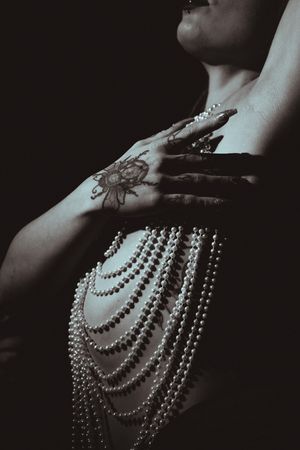 Artistic black and white photo featuring draped pearl strands and decorative hand tattoo.