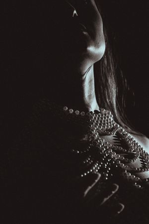 Artistic silhouette photograph showing delicate beaded jewelry draping against a dark background in dramatic lighting.