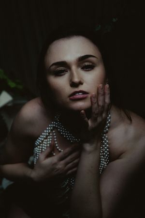 Atmospheric portrait featuring pearl necklaces and dramatic shadowy lighting in a dark setting.