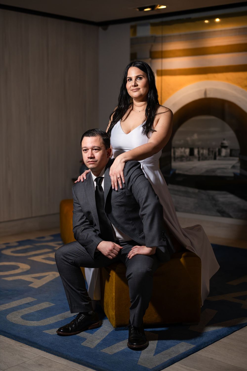 A stylish couple poses dramatically in a hotel lobby with architectural details.