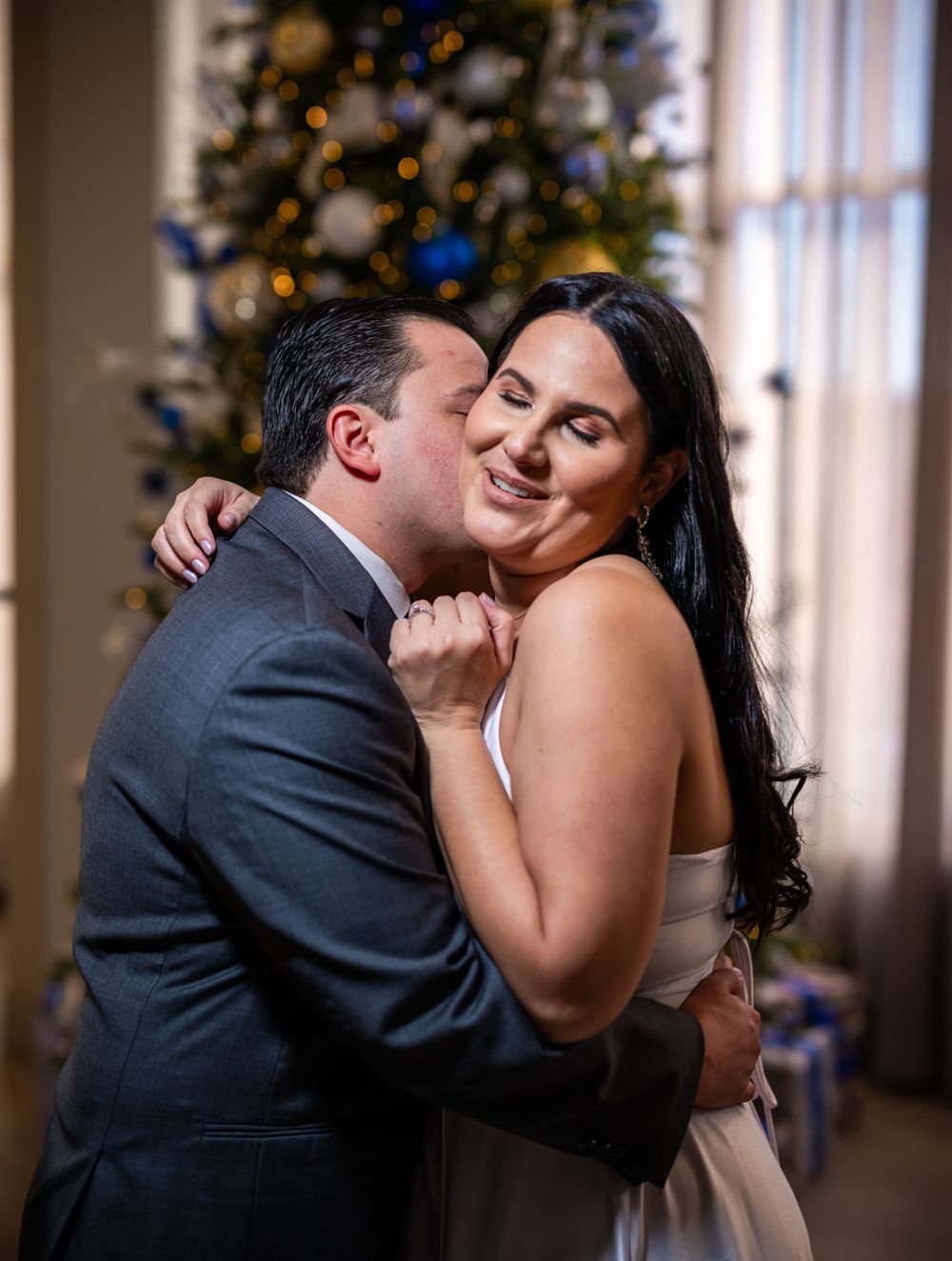 A tender wedding moment captured in front of a decorated Christmas tree with the couple sharing an intimate kiss.