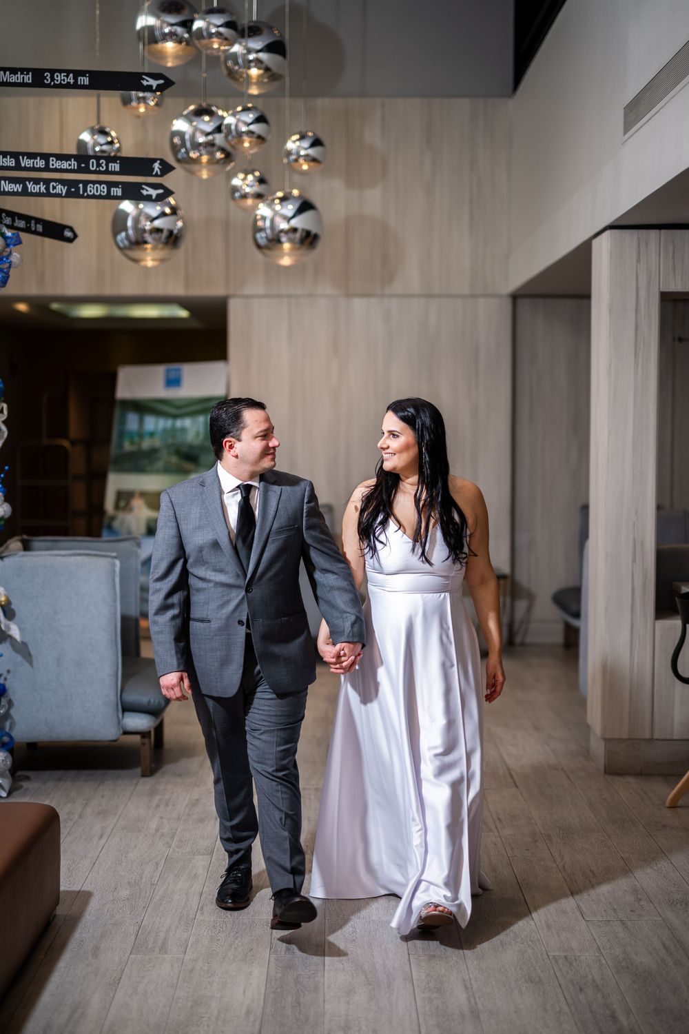 Couple walking hand in hand through modern venue with hanging metallic light fixtures.
