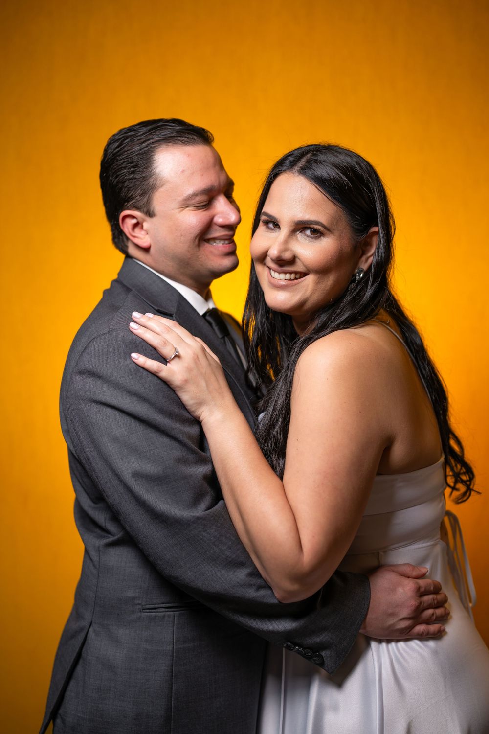 Romantic portrait of newlyweds embracing against vibrant orange background.
