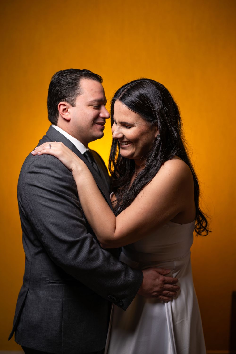 Intimate portrait of couple in formal attire sharing a close moment against warm orange backdrop.