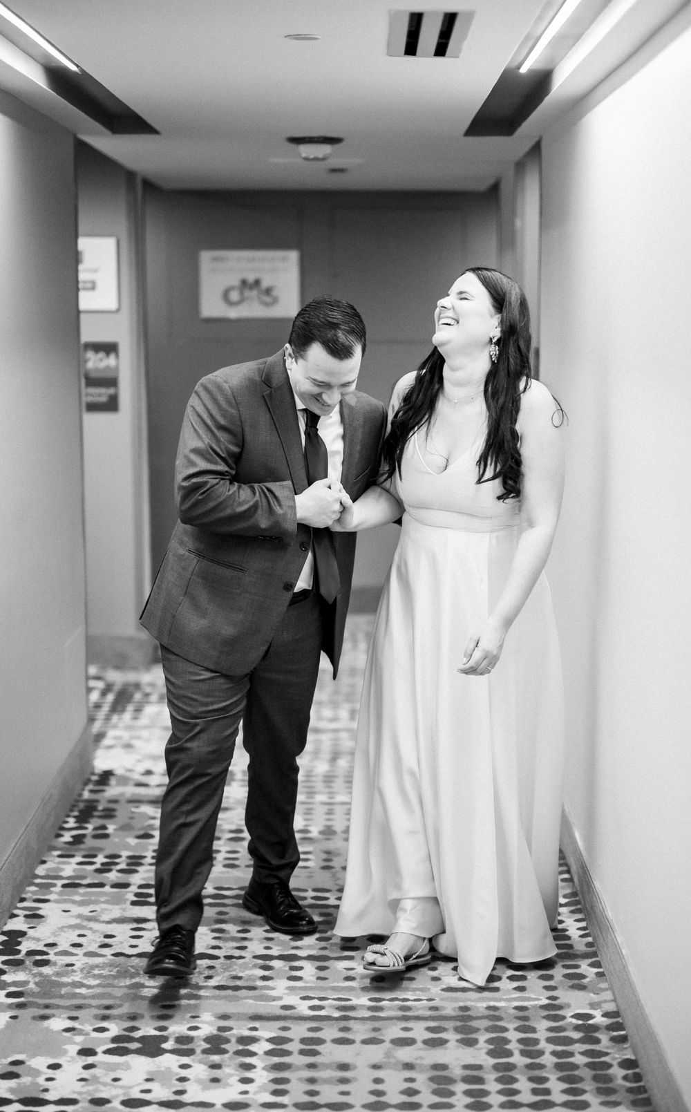 Black and white photo of couple laughing together in hotel hallway.