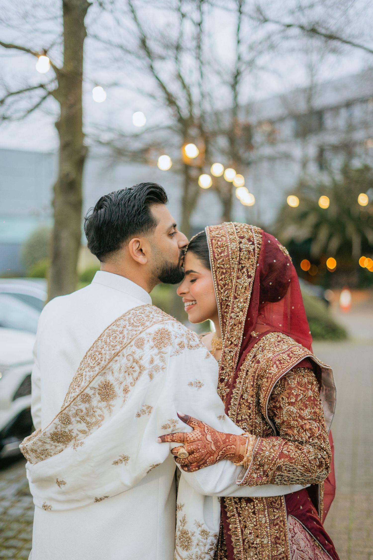 Couple in red and striped traditional outfits pose by wooden staircase railing.