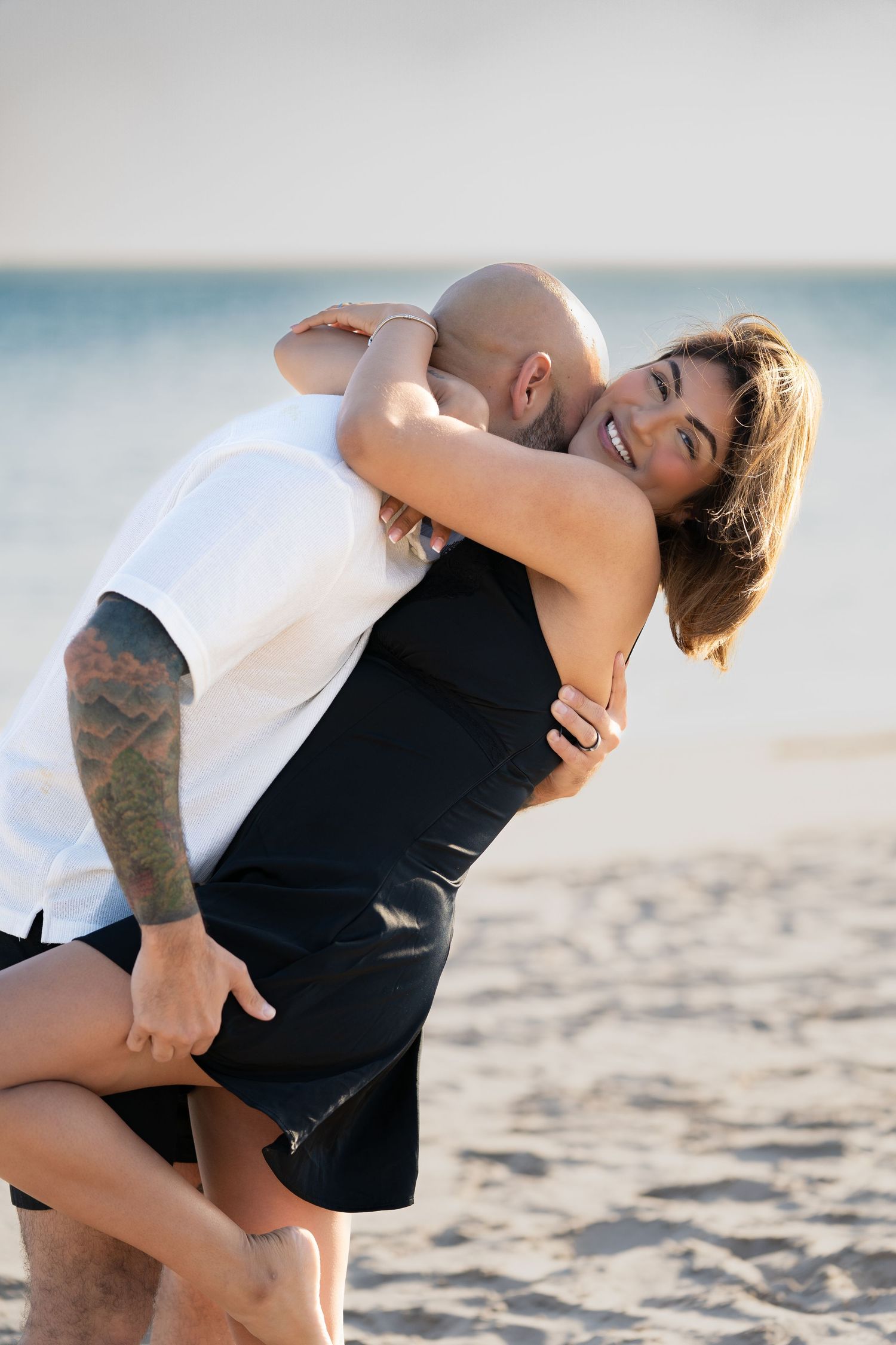 A playful couple embracing on a sunny beach with ocean in background.