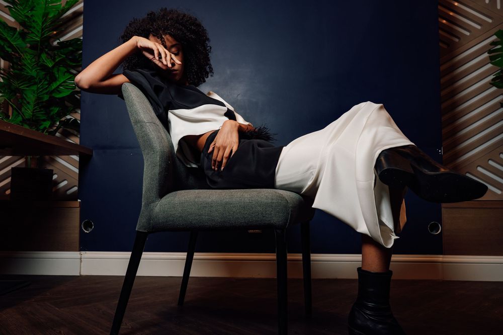 Dramatic fashion pose on dark couch highlighting contrast between black and white garments.