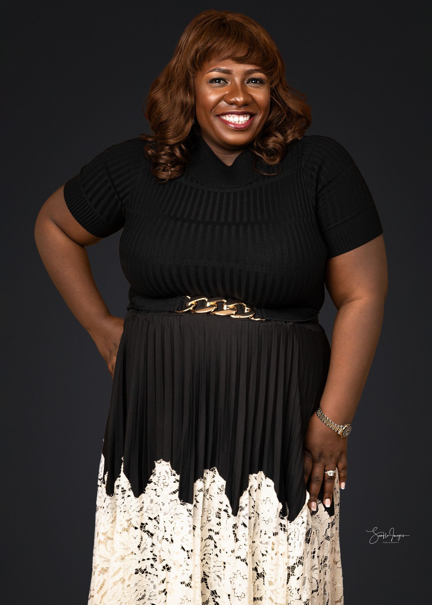 Portrait of someone wearing a black ribbed dress with white lace detail at the bottom and a gold chain belt accent.