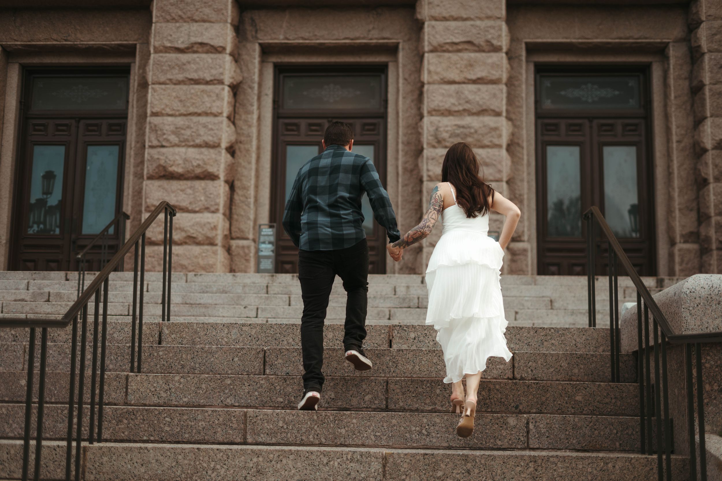 Couple ascending stone steps together while holding hands at a historic building entrance.