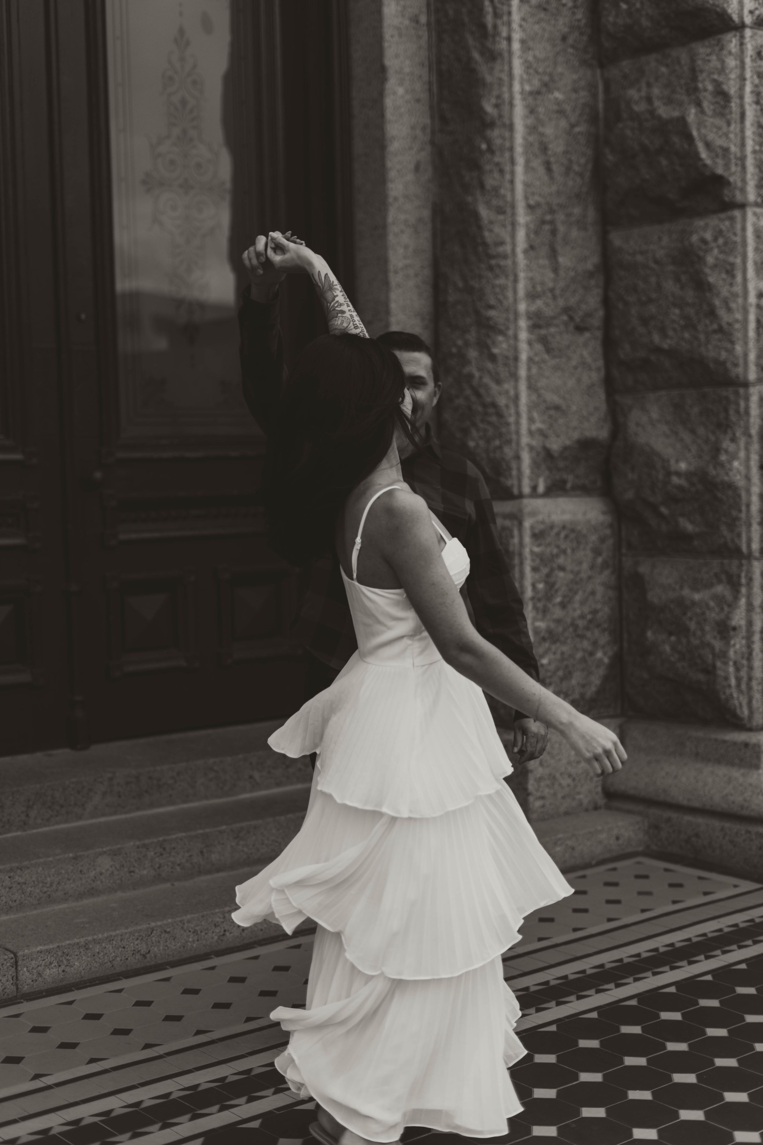 Woman in flowing white tiered dress twirling on historic building steps.