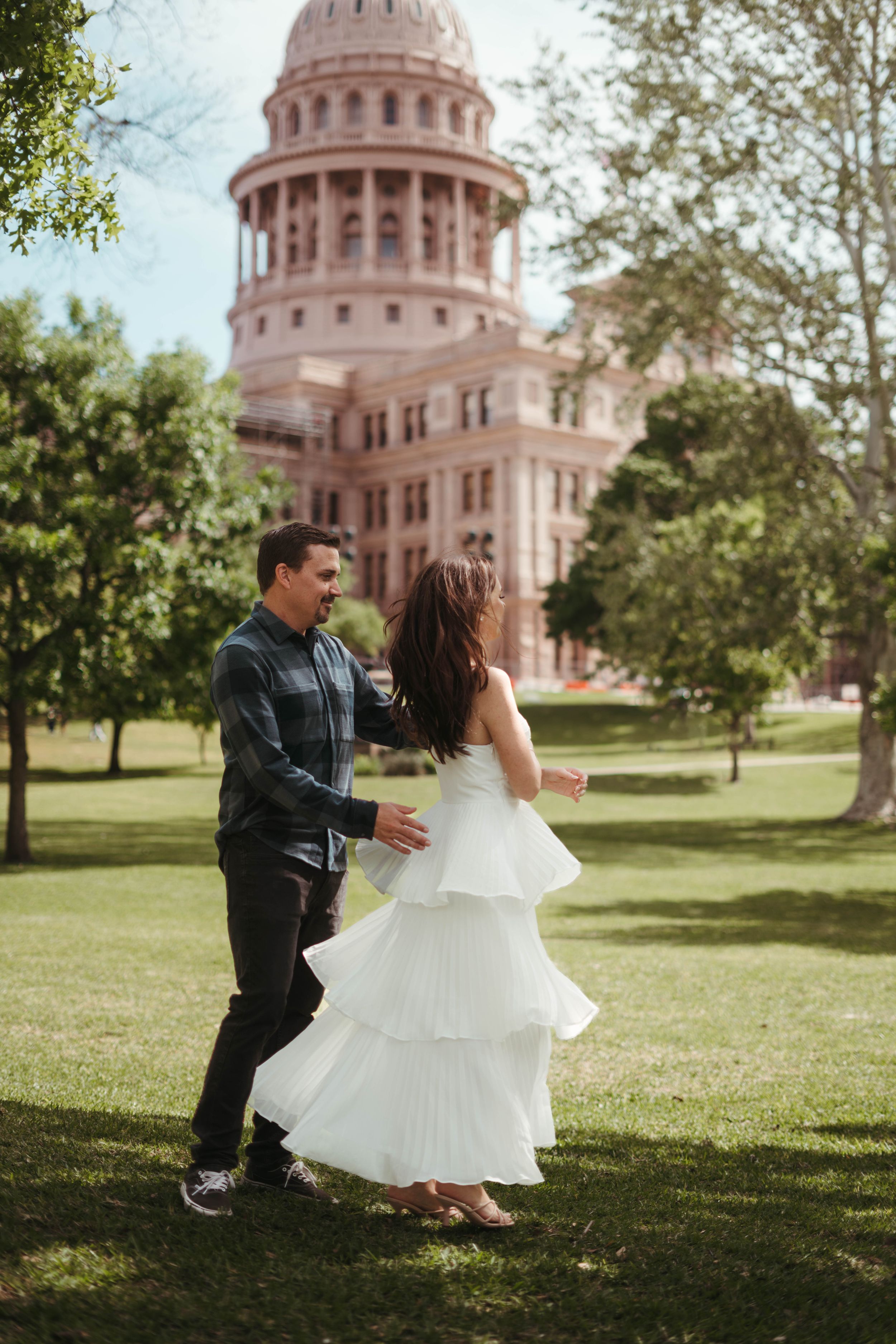 Couple dancing on lawn with Texas State Capitol building in background.