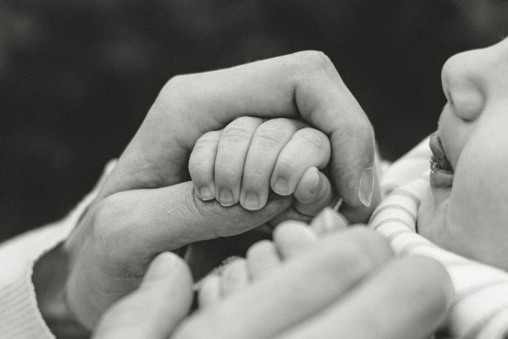 Intimate black and white close-up of hands gently holding a baby's tiny hand.