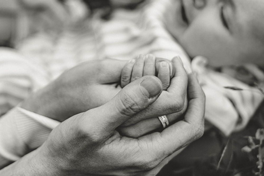 Close-up black and white image of adult and baby hands tenderly touching in an intimate moment of connection.