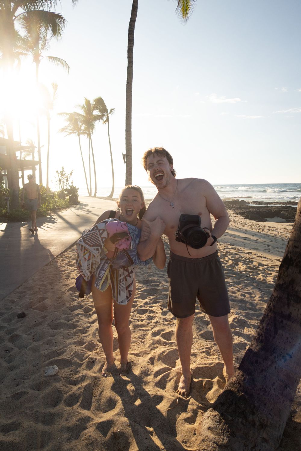 Two people enjoying a sunny beach with palm trees and ocean in the background.