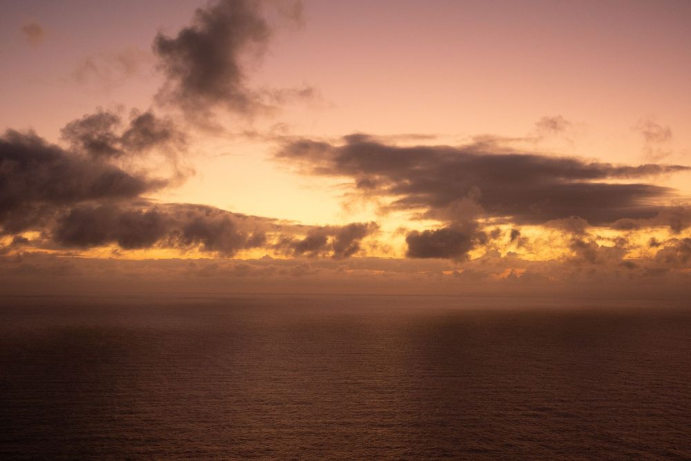 Dramatic sunset over ocean horizon with golden clouds and dark water reflecting warm light.