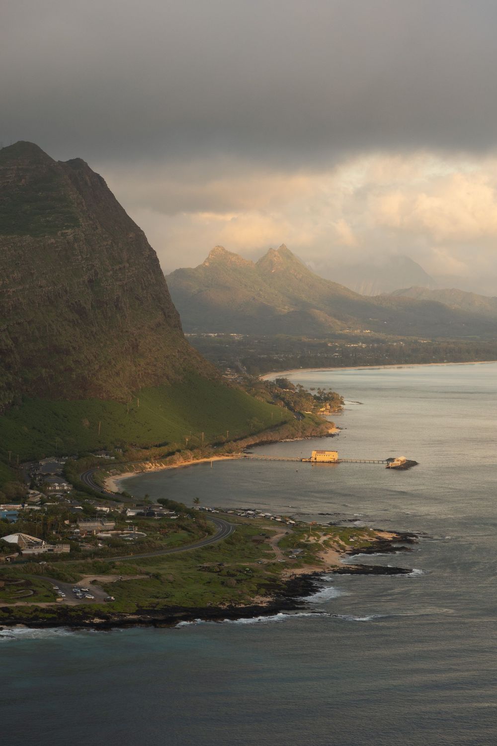 Dramatic coastal landscape in Hawaii with steep mountain cliffs and tranquil bay waters during golden hour.