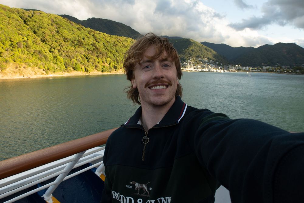 Scenic selfie captured on a boat with green hills and water in the background.