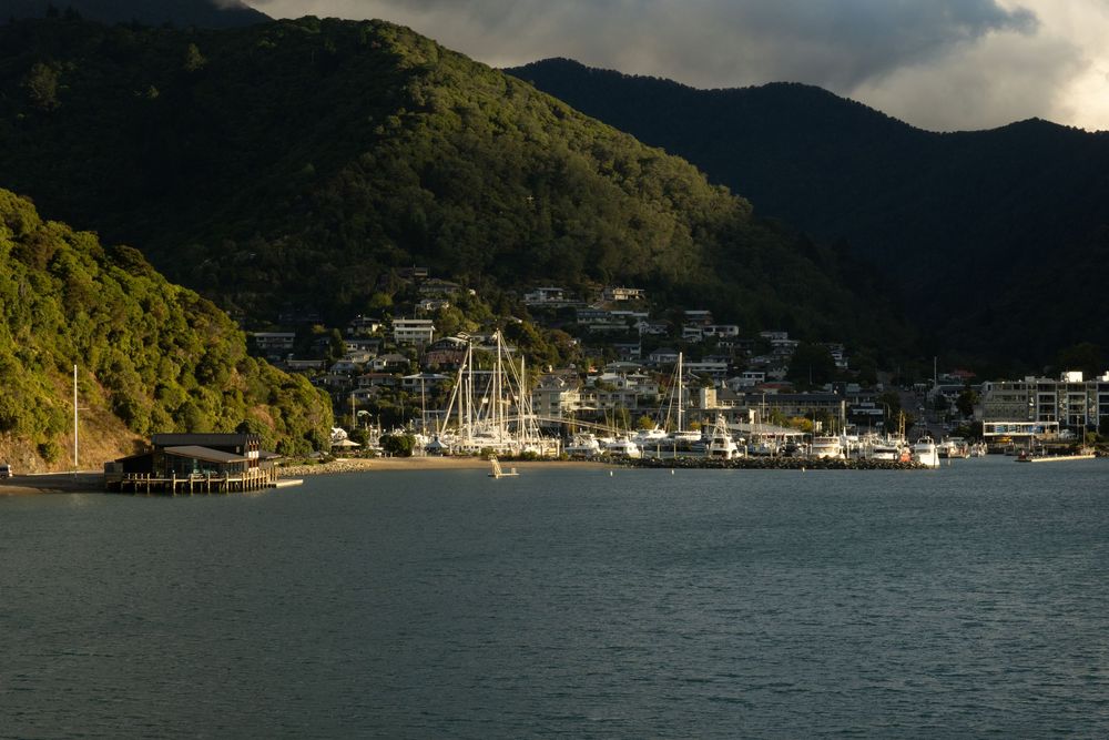Scenic harbor marina with boats docked against mountainous backdrop during golden hour.