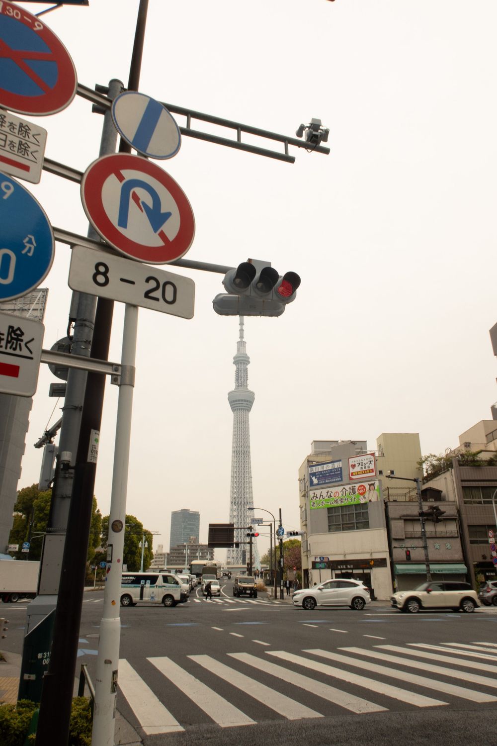 View of Tokyo Skytree tower from a street intersection with traffic signs and zebra crossing in the foreground.