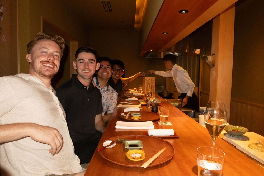 People dining at a Japanese restaurant counter with plates of food and drinks.