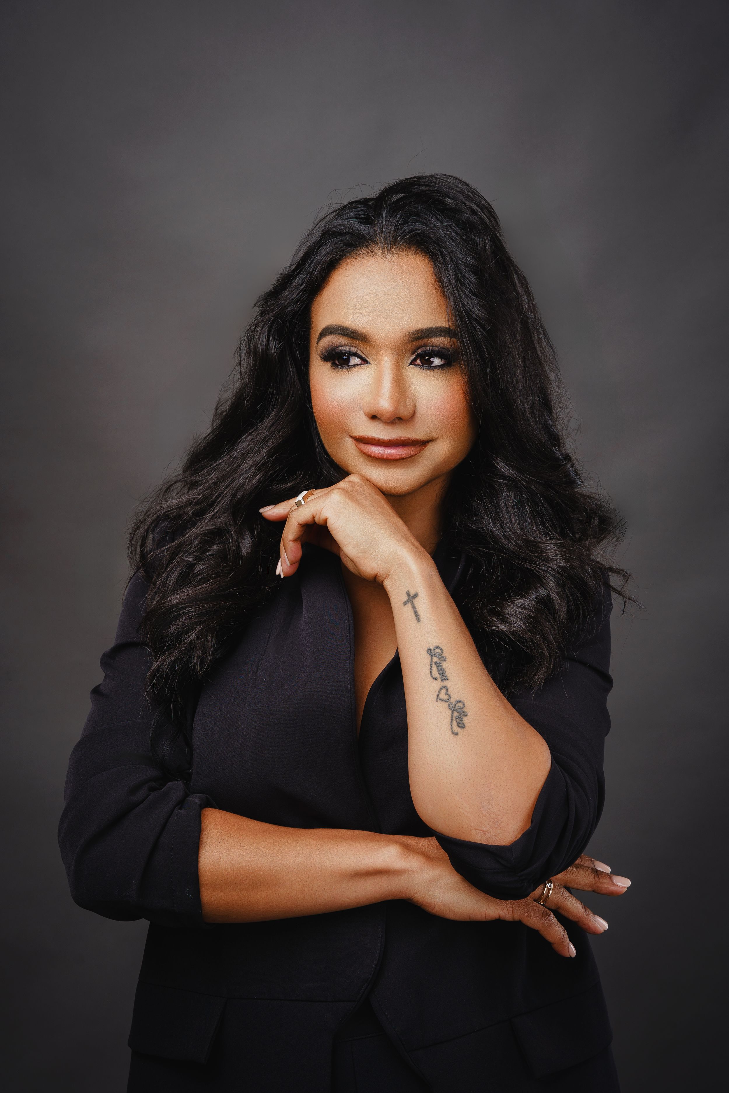 Professional studio portrait with black blazer against dark grey background.