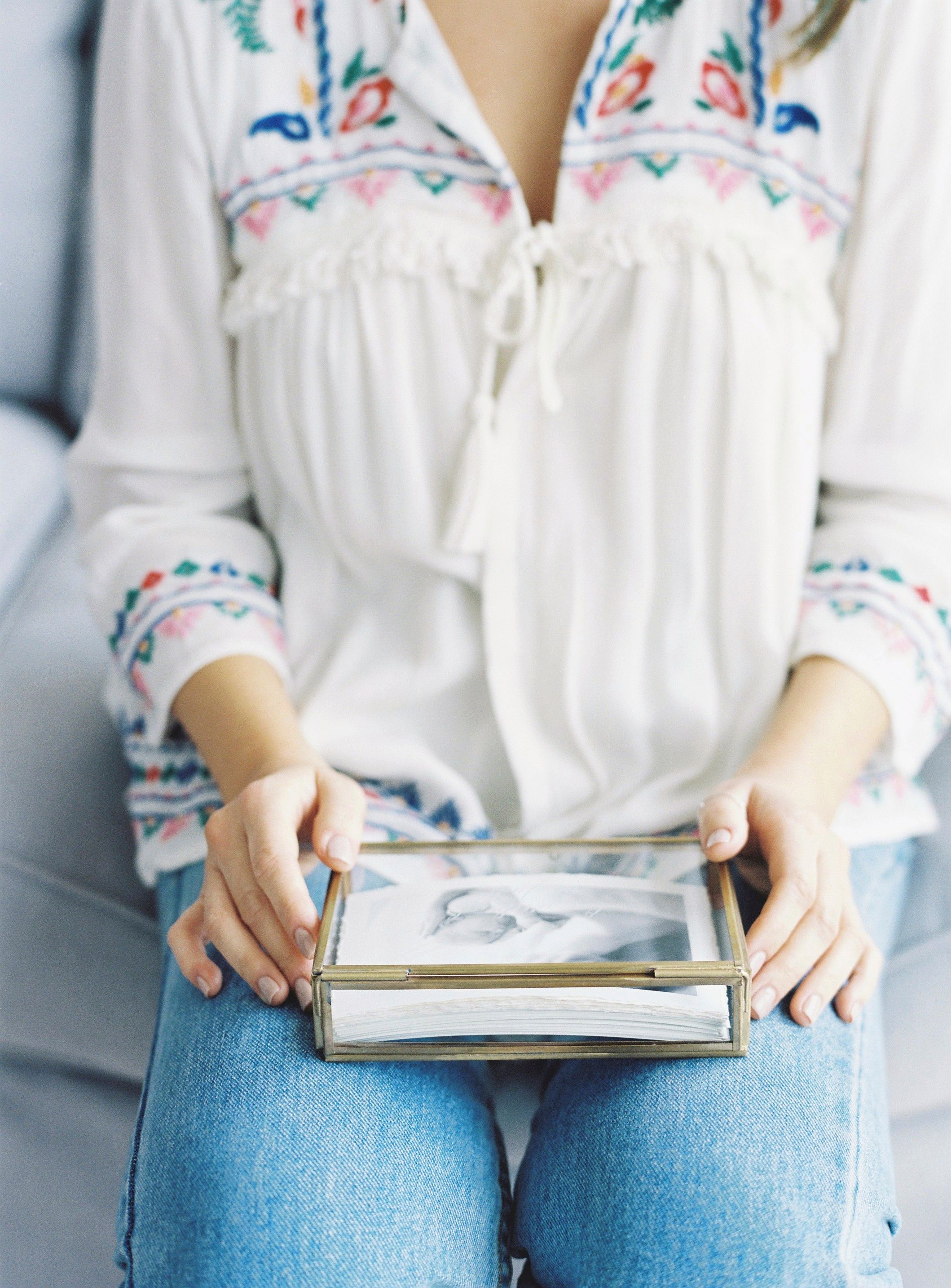 Person in embroidered white top holding photo album while sitting in jeans.