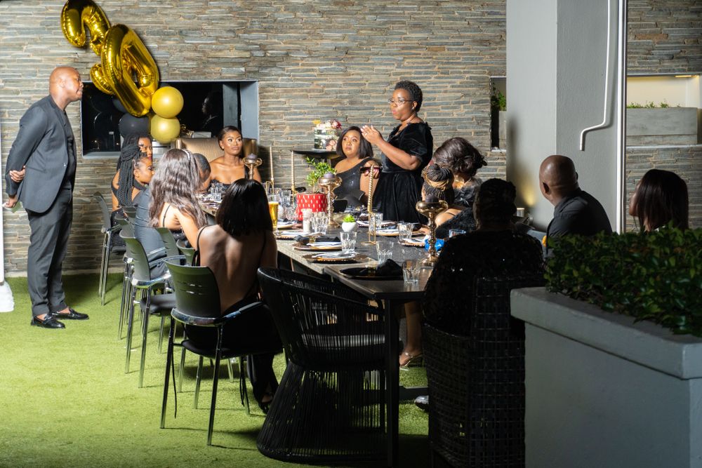 Outdoor celebration dinner with guests seated at a long table under decorative lighting.