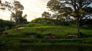 Hobbit houses built into green hillsides at sunset in New Zealand's Hobbiton Movie Set.