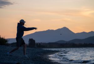 Silhouettes of mountains against an orange sunset sky over a peaceful beach.