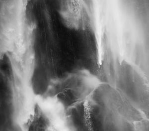 Misty waterfall cascading down rocky cliff face in black and white.