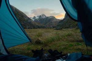 Teal camping tents set up in a mountainous landscape during sunset with snow-capped peaks in the distance.