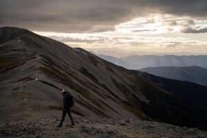 Rocky mountain trail winding through rugged terrain under cloudy skies at dusk.