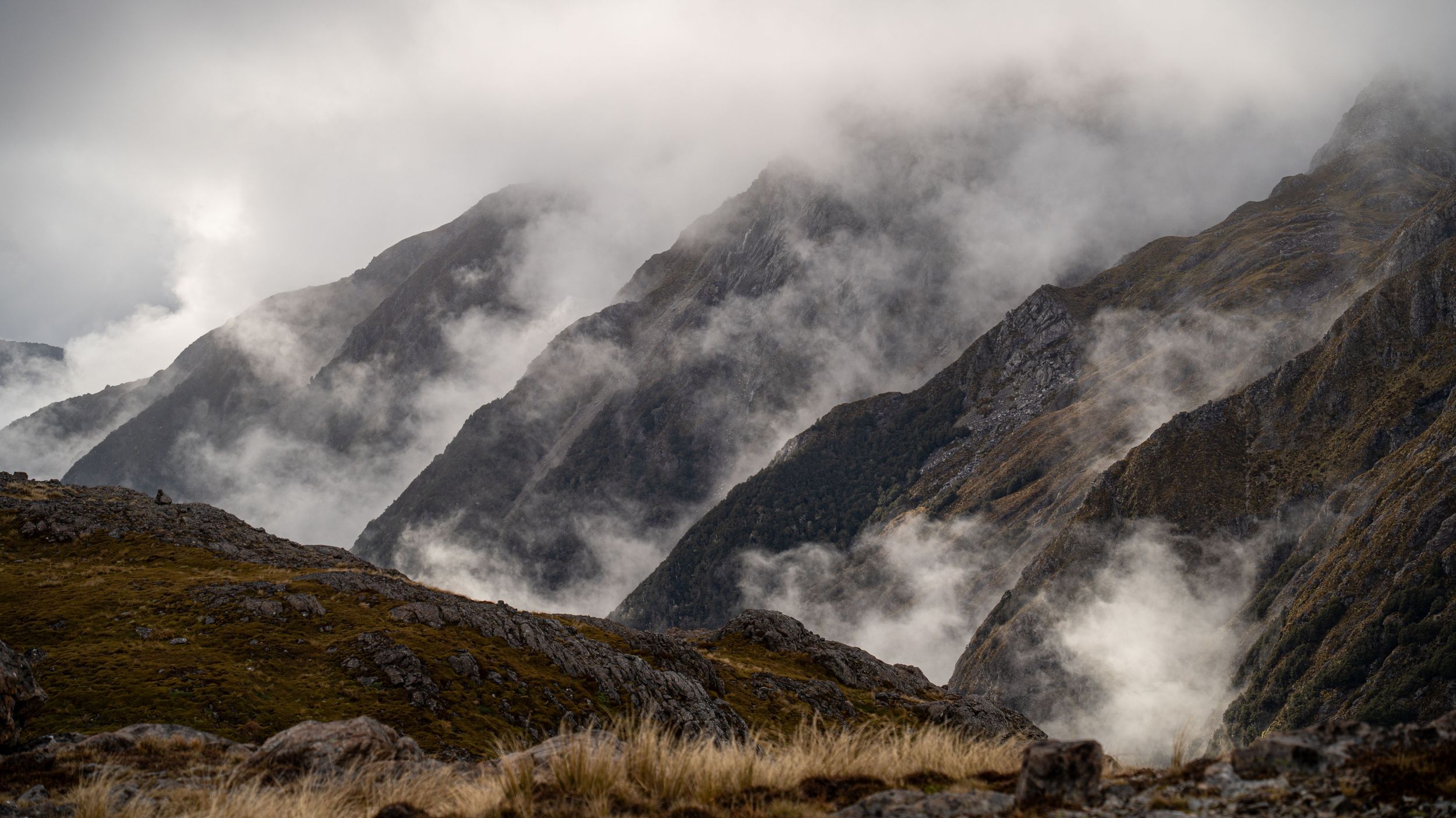 Misty mountain peaks shrouded in dramatic clouds during sunrise.