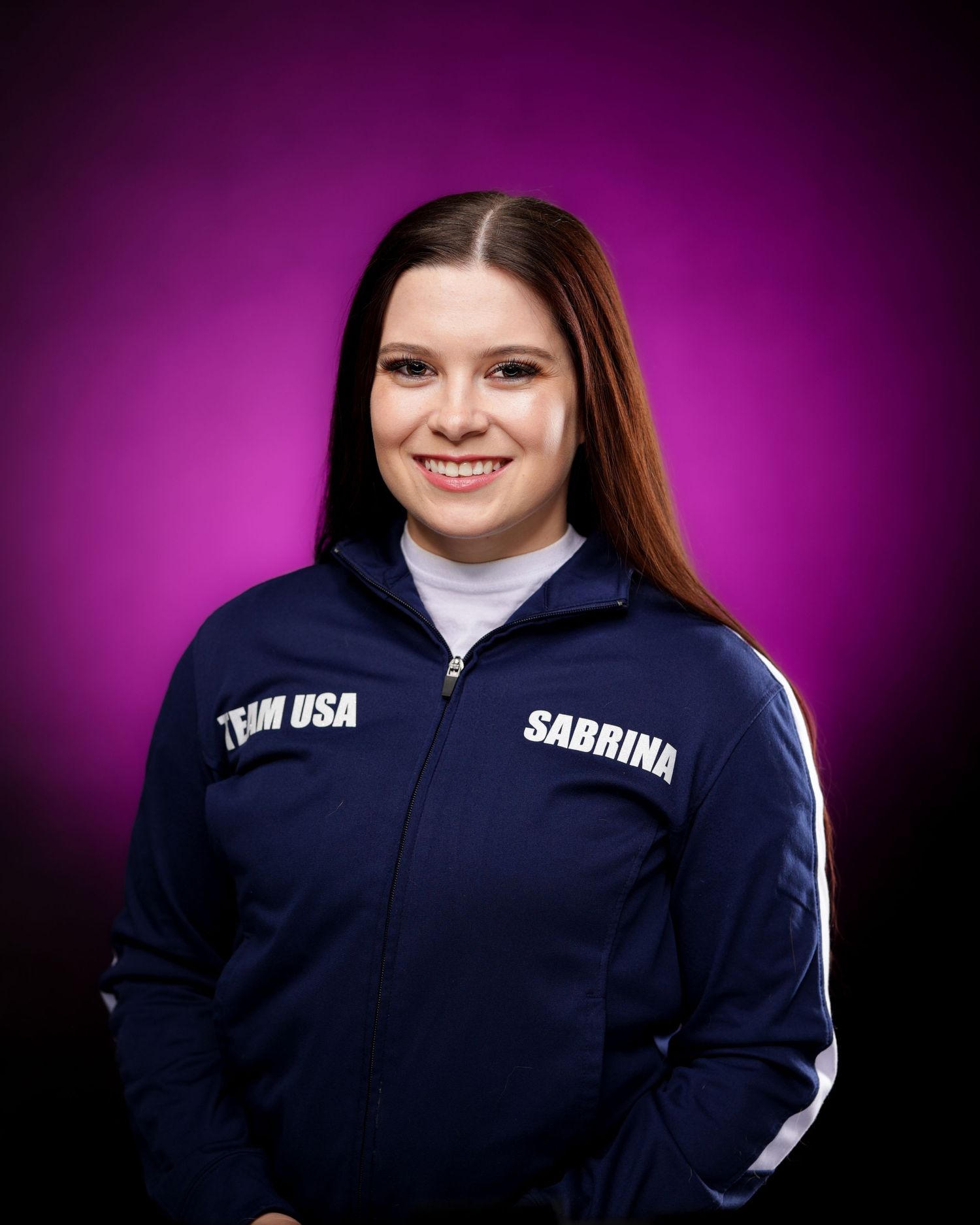 Team USA member in navy blue athletic jacket poses against purple backdrop.