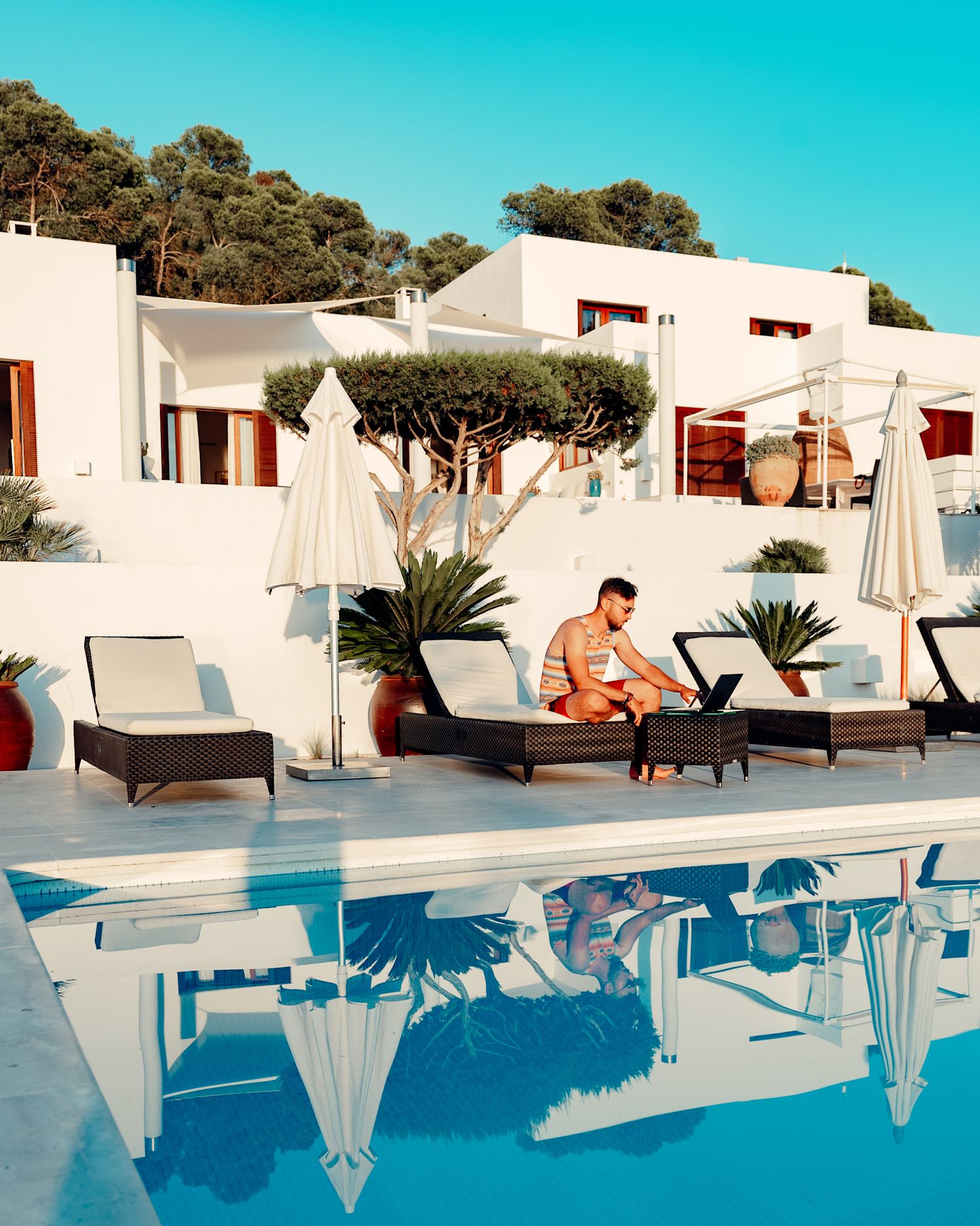 Luxurious cabana loungers arranged by a turquoise swimming pool with white buildings on a sunny Mediterranean day.