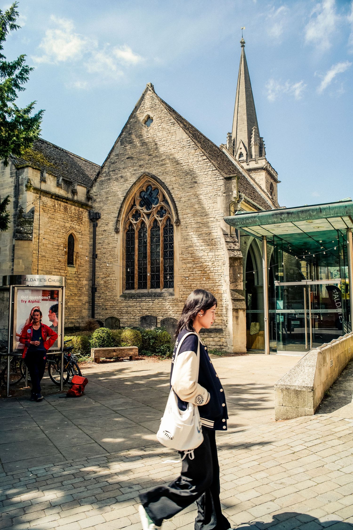 Gothic stone church with large stained glass window and modern glass entrance extension.
