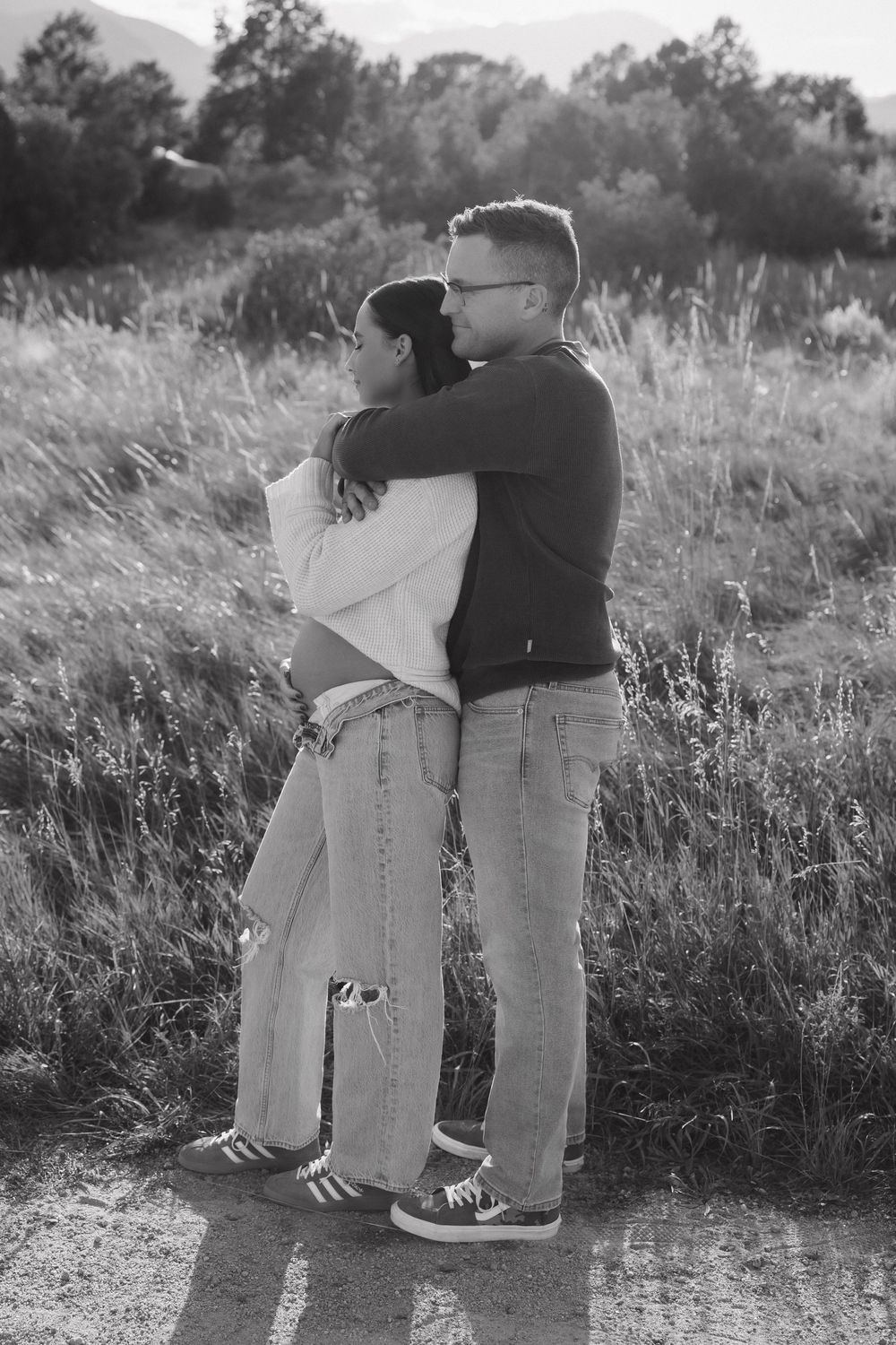 Black and white photo of a couple in casual denim sharing an intimate moment on a nature trail.