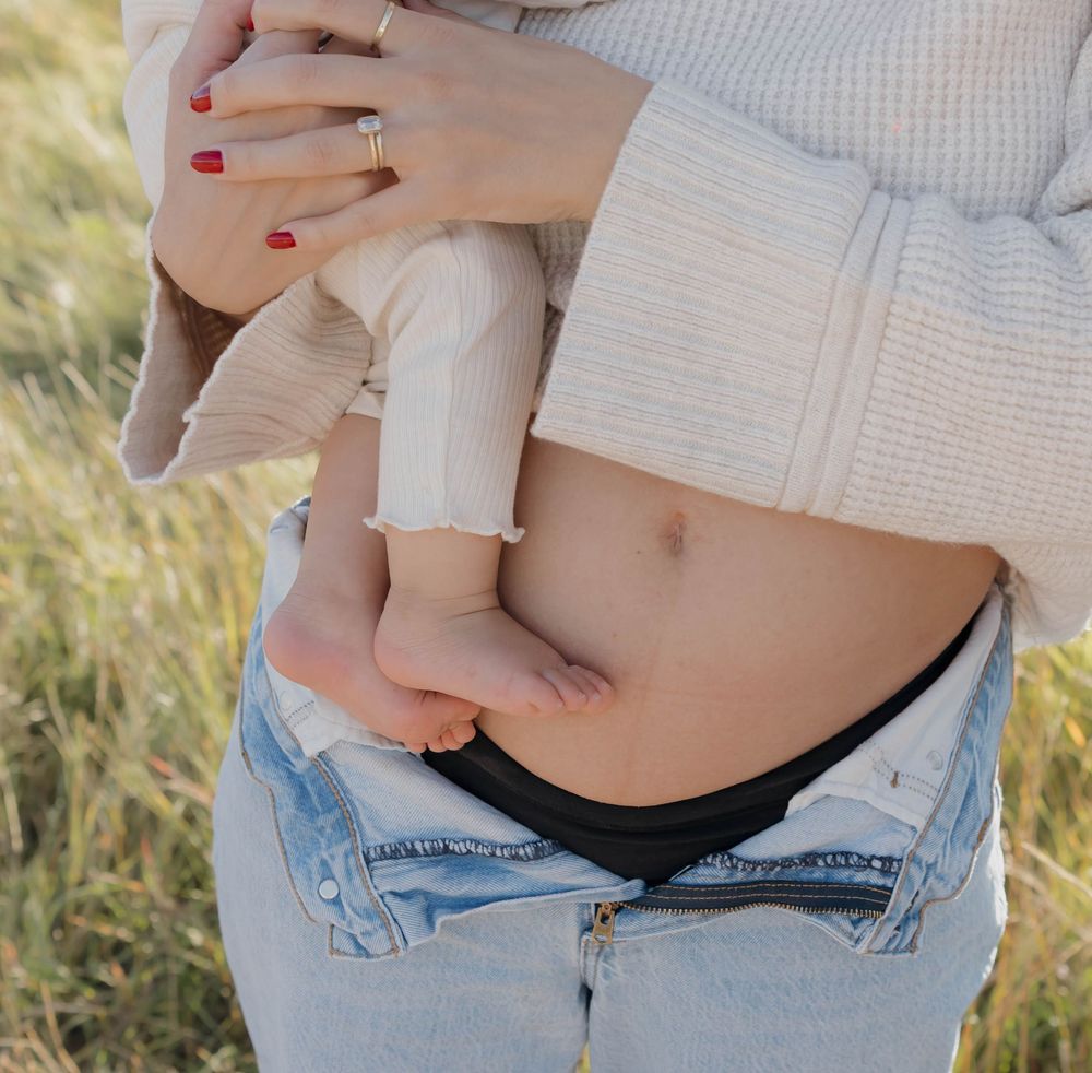 Close-up view of a pregnant belly with hands holding ultrasound photos against light denim jeans.