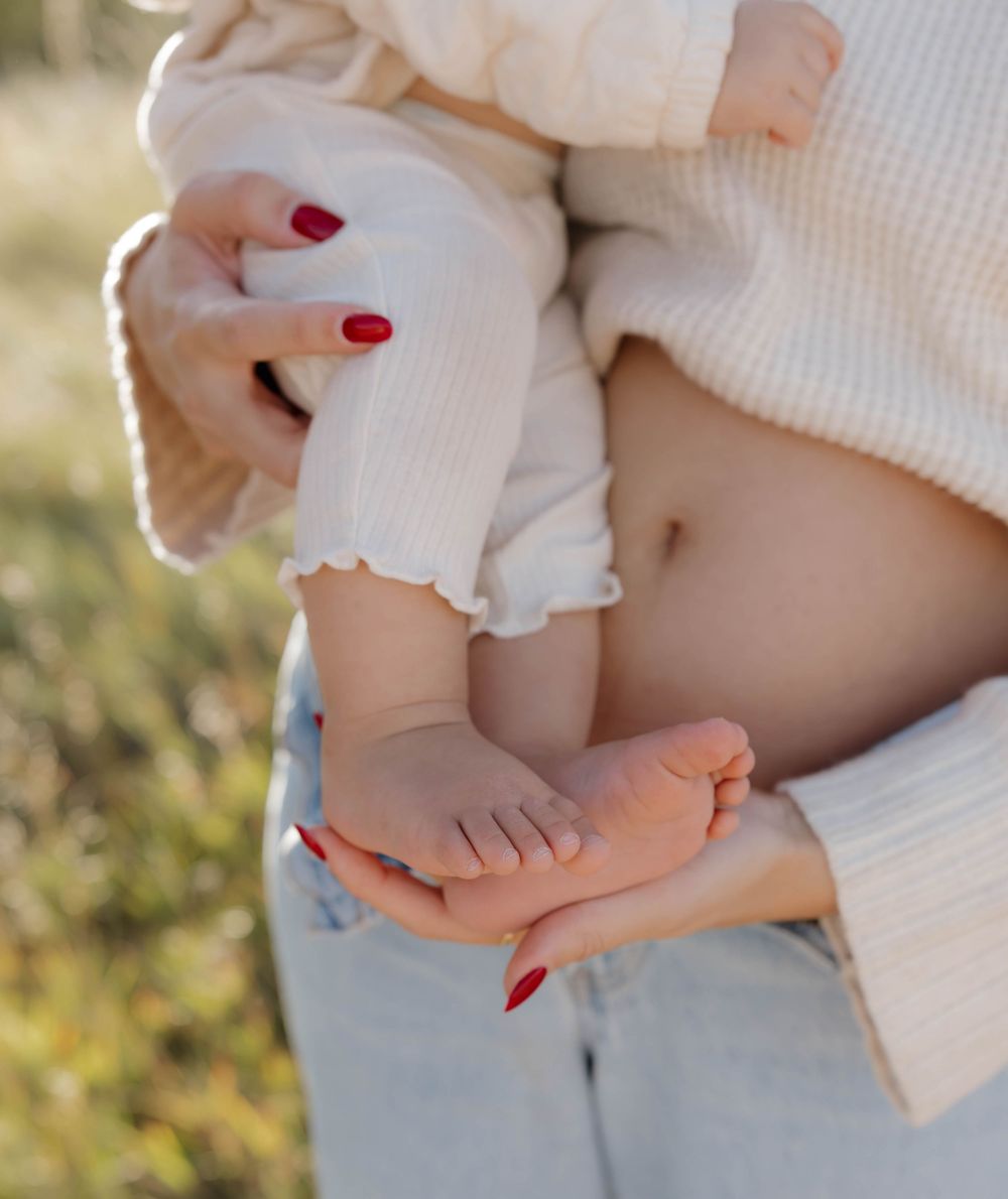 Close-up of hands gently cradling small baby feet against a soft white knit background in natural sunlight.