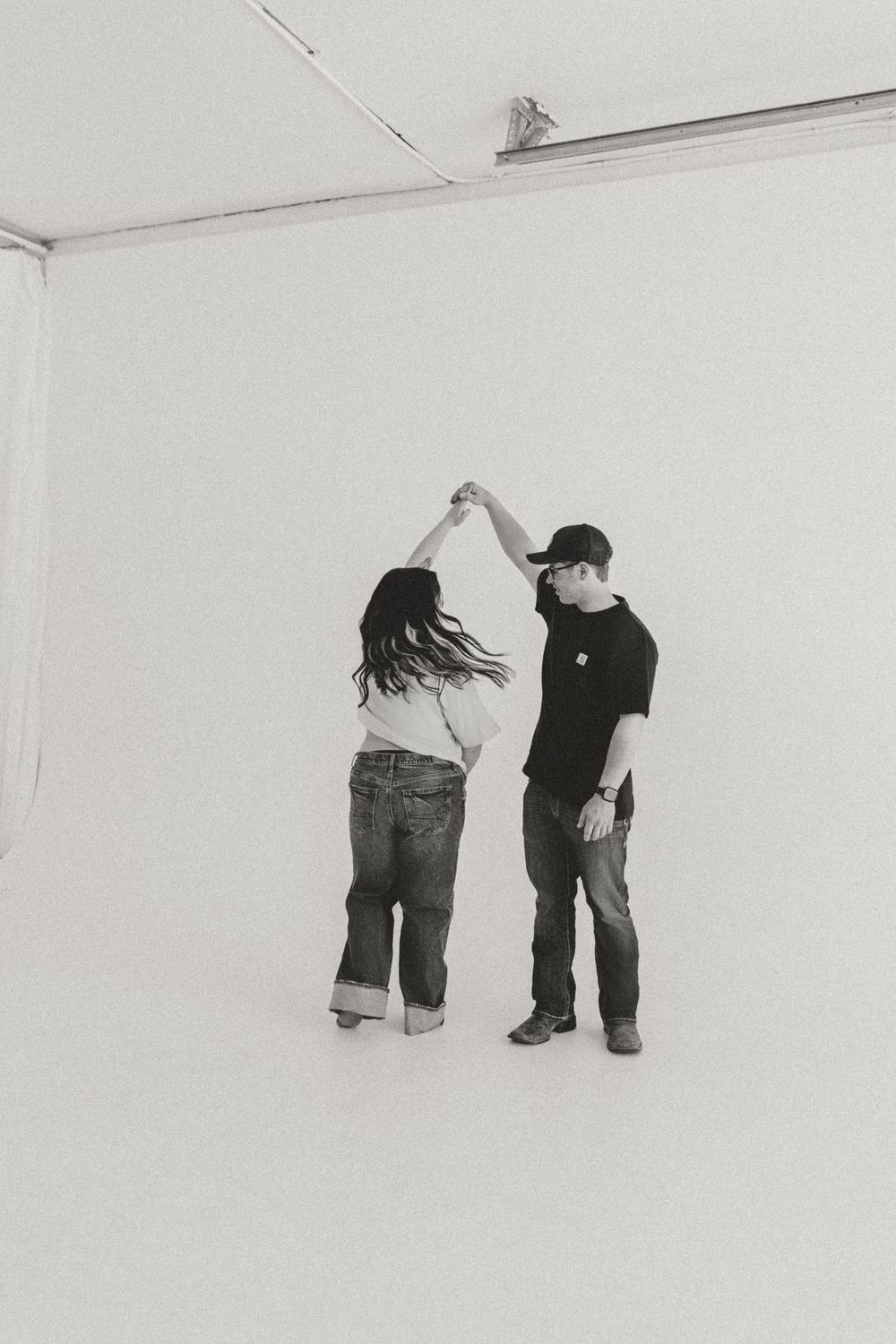 A couple dancing together in a white studio space, captured in black and white photography.