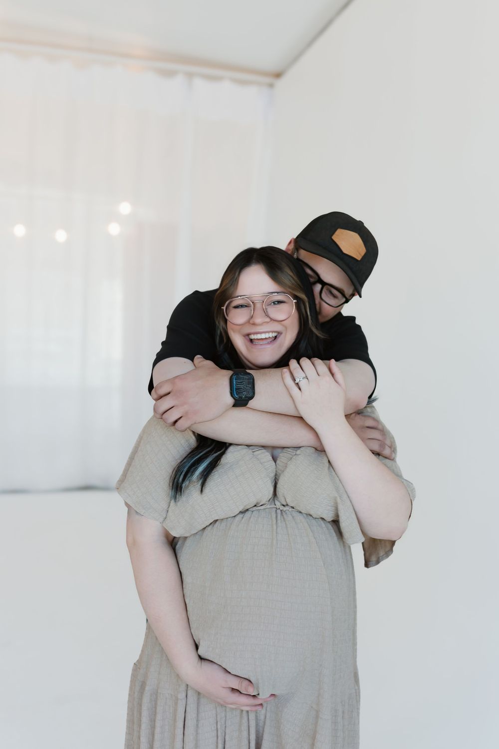 Couple embraces in a bright white room while wearing casual clothes, sharing a joyful moment together.