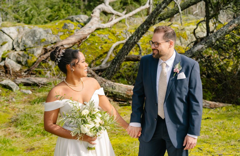 A joyful wedding couple shares a candid moment together outdoors with moss-covered trees and natural scenery.