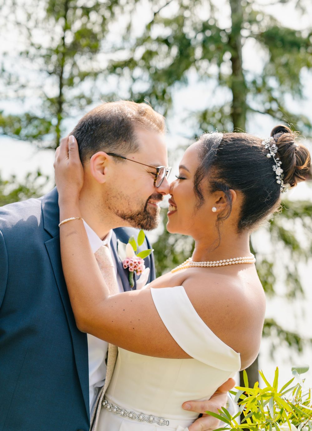 A joyful newlywed couple sharing a romantic outdoor moment with greenery in the background.