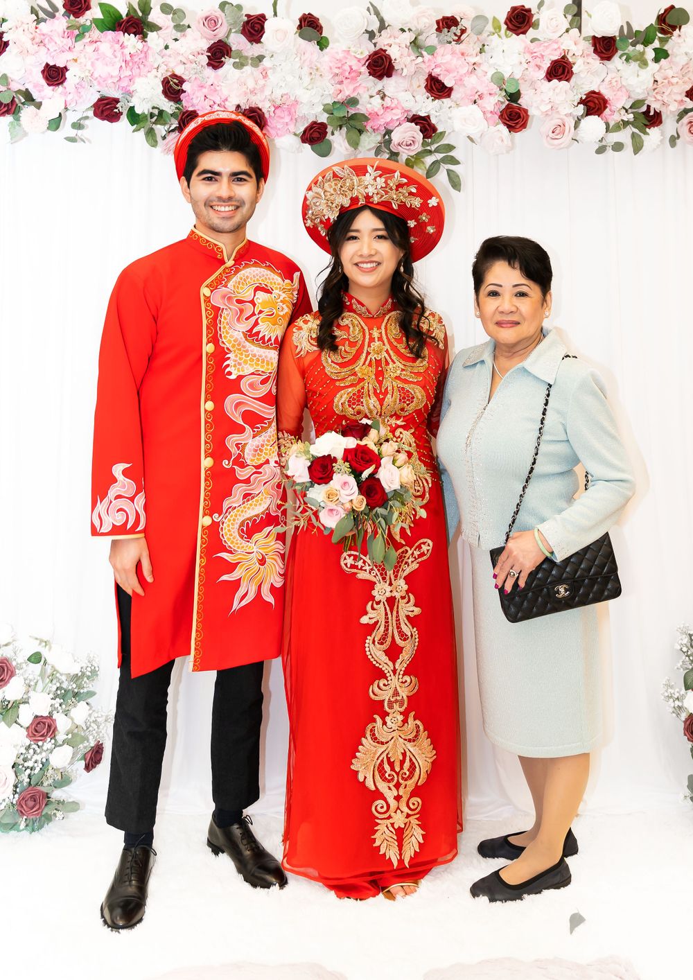 Traditional Vietnamese wedding photo with couple in red ao dai outfits under pink and red floral arch.